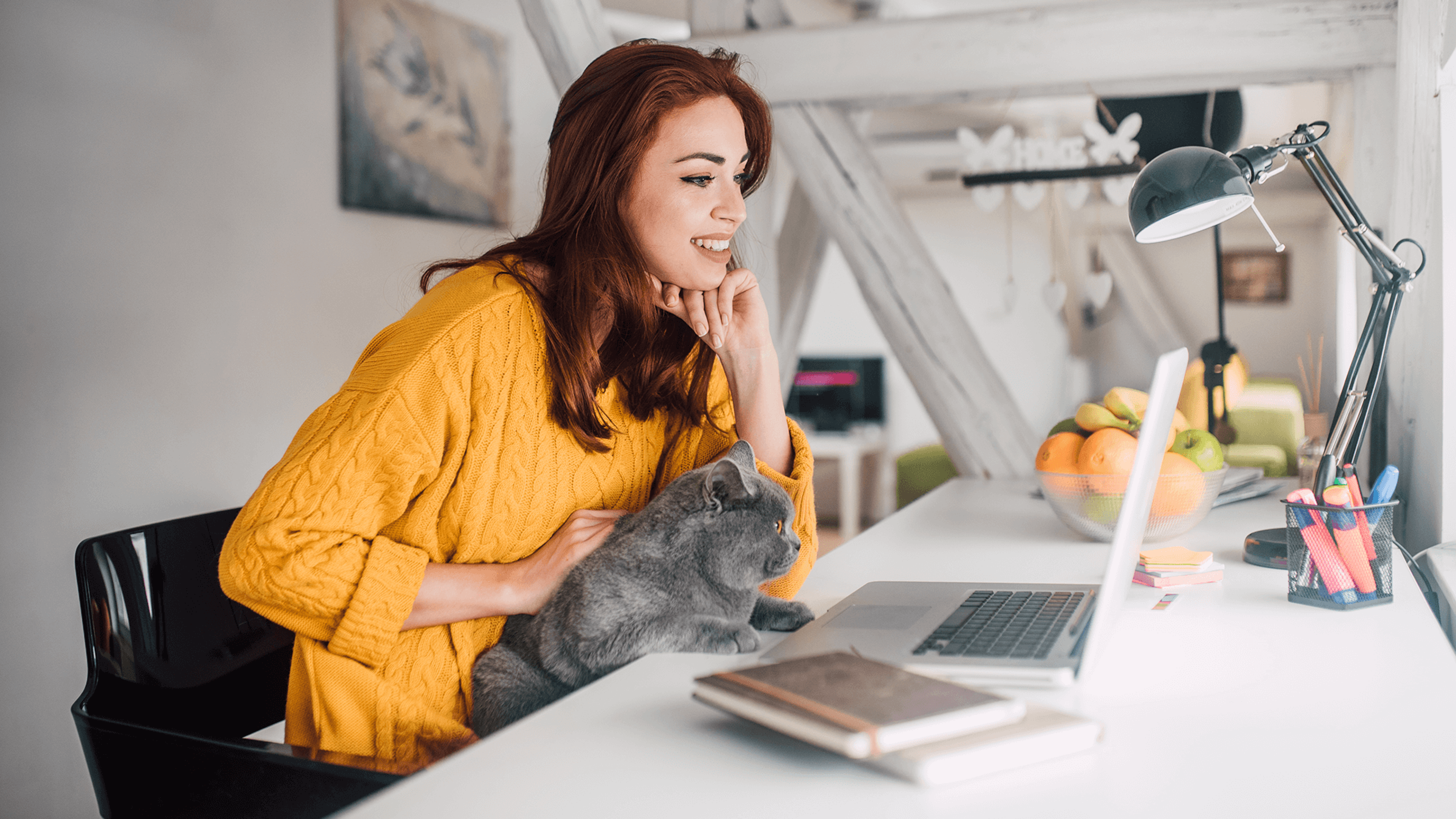 Glückliche Frau mit Katze am Schreibtisch vor Laptop